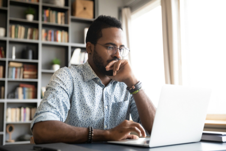 Close up of man sitting at desk, concentrating on research on his laptop.
