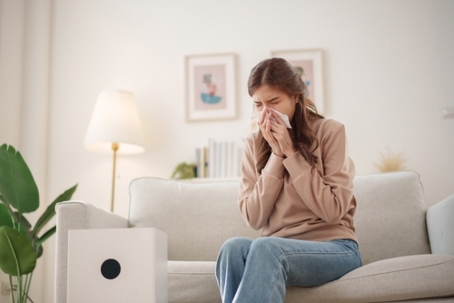 Woman sitting on couch sneezing and holding tissue.