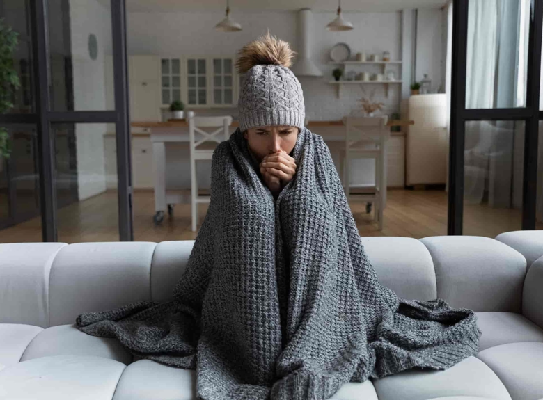 A woman shivering under a blanket